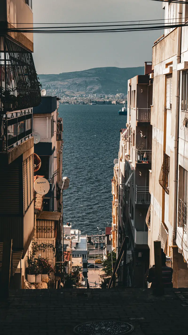 A sloping İzmir street between apartment blocks, opening onto the bay at the bottom
